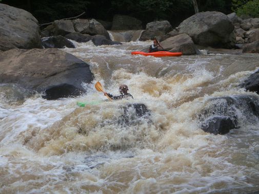 One kayak navigates the churning rapid while a second waits above
