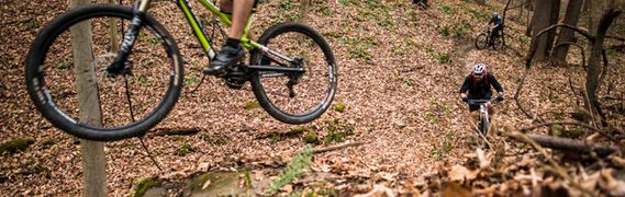 A mountain bike hops over a small jump with another bike following
