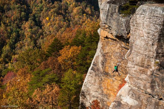 A climber high on a rock face with background trees in full fall colors