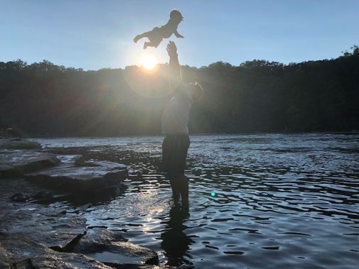 A dad tosses his son in the air next to the Youghiogheny River