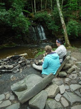Backpackers sit in a campsite near a small waterfall
