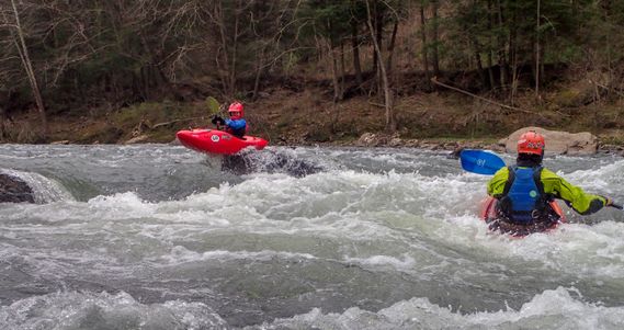 A kayakers paddles over a small drop while another looks on