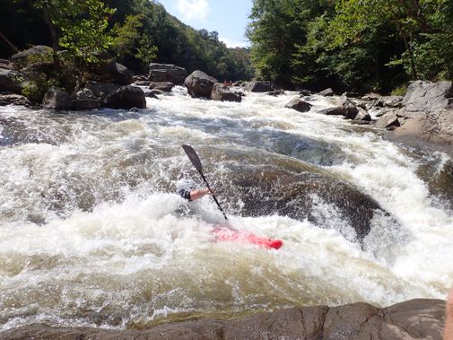 A partially hidden kayaker paddles through a rough rapid on the Upper Yough River