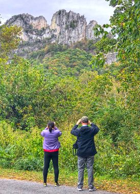 Two people look at Seneca Rocks with binoculars
