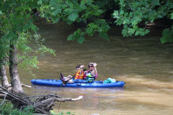 Two people in a kayak waive while floating on the Little Kanawha River