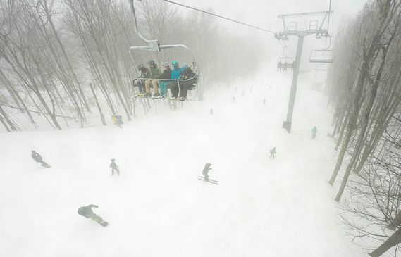 Skiers carve down the slope as a group on the lift watches