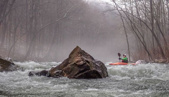 A kayaker paddles around a large rock on the Savage River