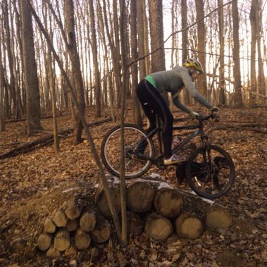 A mountain biker rides over a log pile at White Park