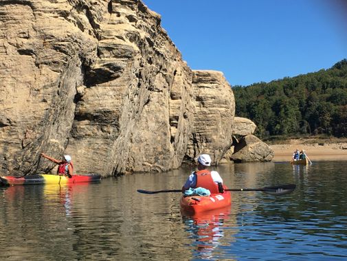 Kayakers and a canoe paddle next to cliffs at Tygart Lake