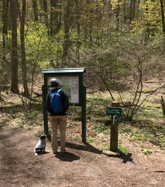 A hiker and their dog look at the trailhead sign at Coopers Rock
