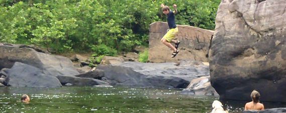 One person jumping off a rock into the Cheat River while others swim below