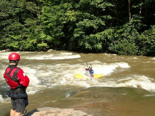 A son watches his father kayak through a rapid on Big Sandy Creek