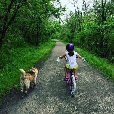 A child on a bike rides beside a dog on the rail trail