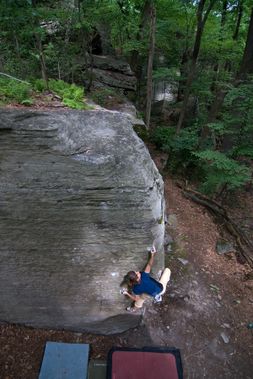 A person reaching high for a hold on a boulder problem