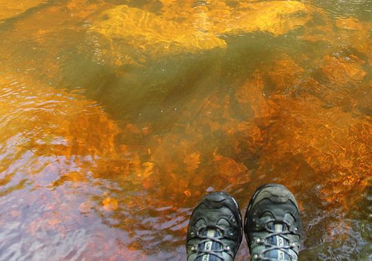 The tannin red color of the creek below resting boots
